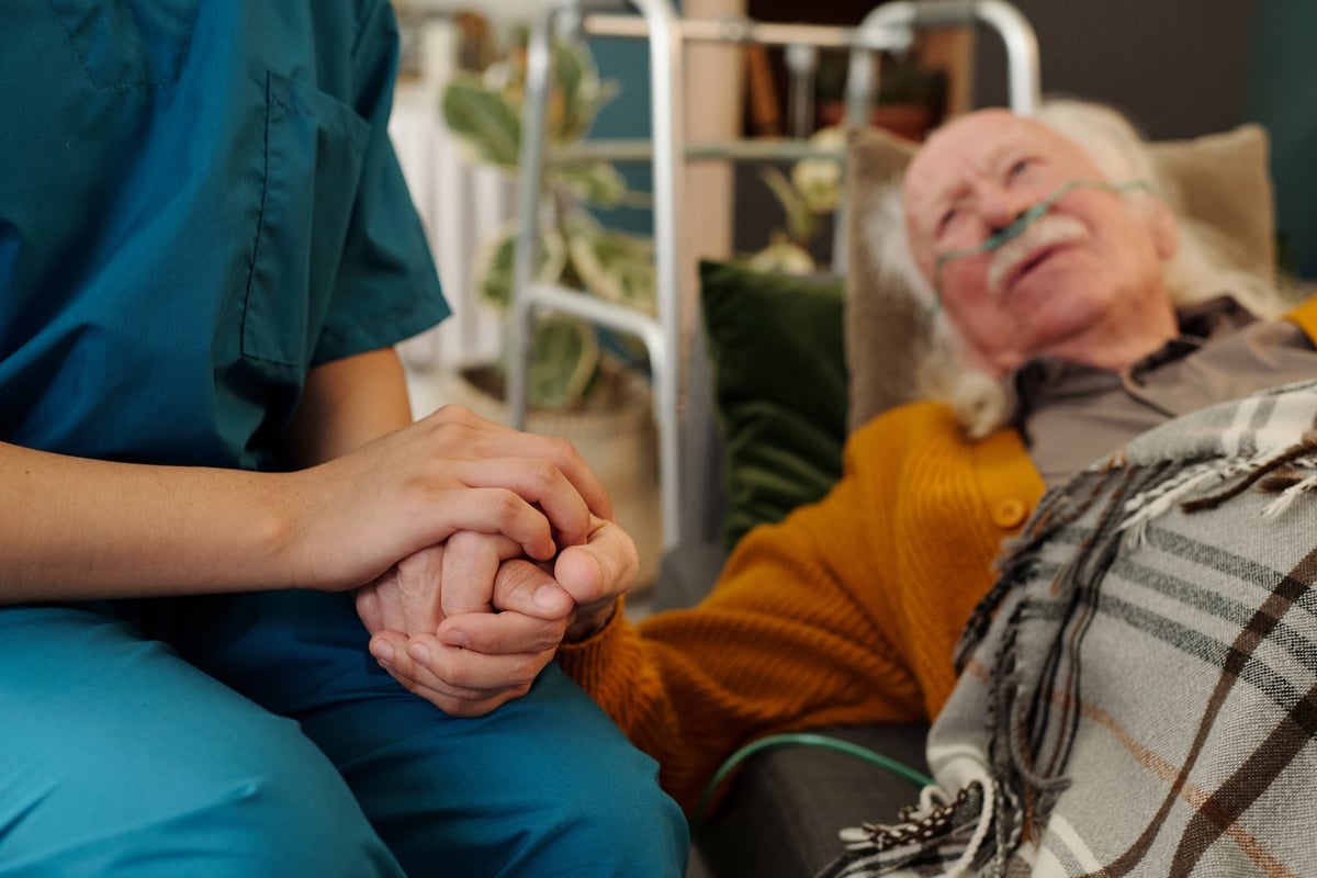 Senior patient with oxygen tube holding hands with caregiver